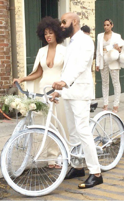 Solange Knowles and Alan Ferguson riding white bicycles together on their wedding day in New Orleans, dressed in all-white wedding outfits.