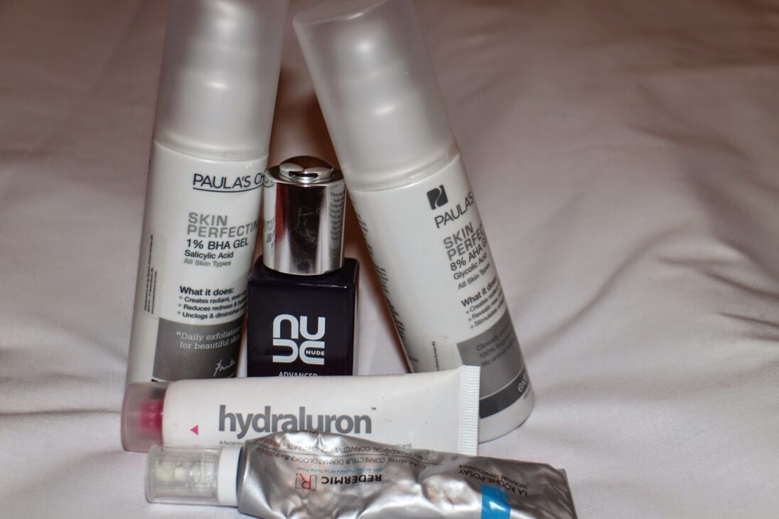 A collection of skincare bottles including Nude Skincare serum, Paula's Choice gels, and Hydraluron.
