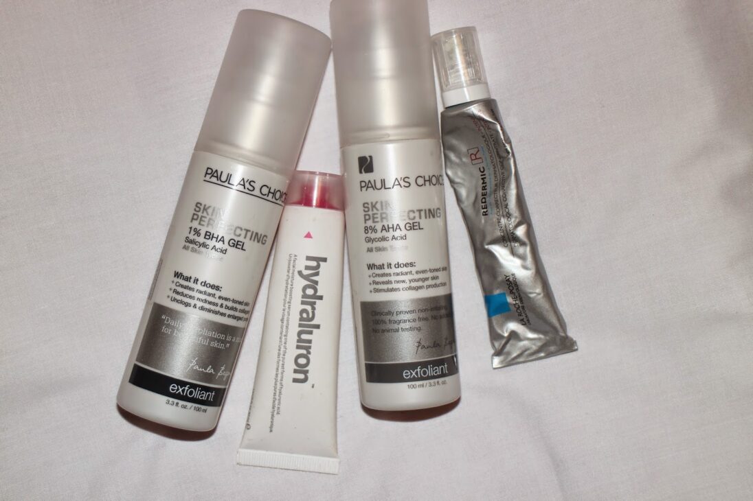 Paula’s Choice BHA and AHA gels, Hydraluron serum, and La Roche-Posay Redermic tube on a white surface.
