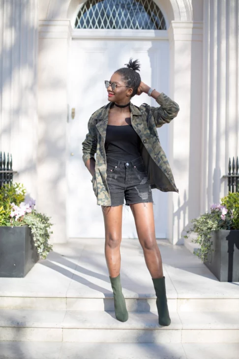 Woman wearing tortoiseshell cat-eye sunglasses and an unlined camouflage jacket posing outdoors in London