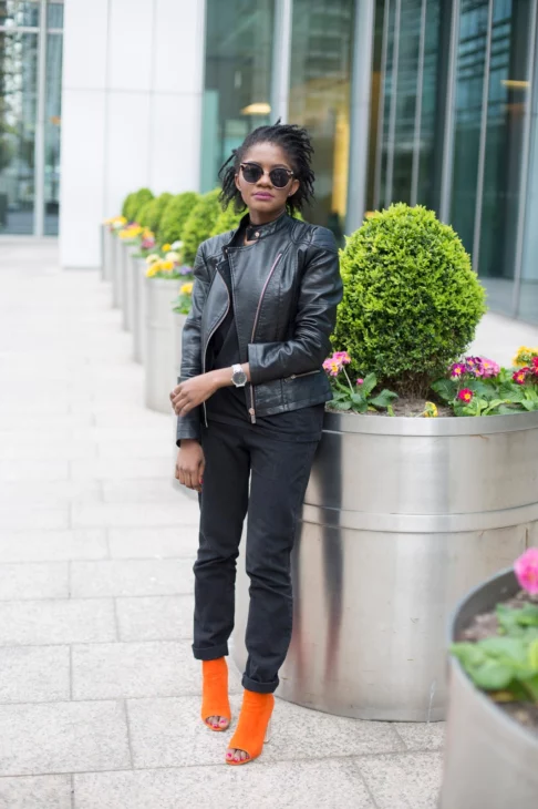 Full-length street style portrait wearing high-waisted black jeans, leather biker jacket, and bright orange heels in London