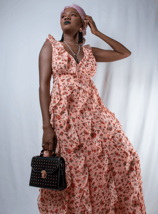 Mariama in a tiered peach floral ruffle dress holding a black handbag for prom outfit inspiration